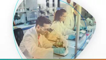 Científicos en laboratorio usando microscopio y tomando notas.
