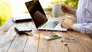 Persona trabajando en un portátil al aire libre, sosteniendo una taza de café.