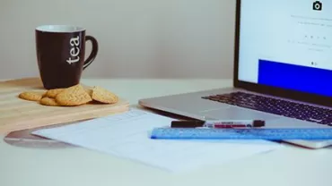 Mesa con taza de té, galletas, portátil y papel.