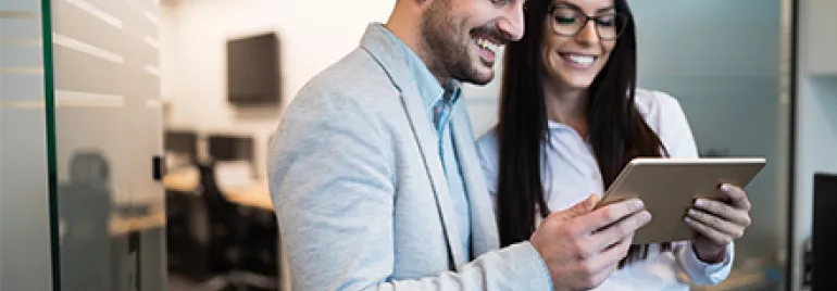 Dos personas sonriendo mientras miran una tablet en una oficina.