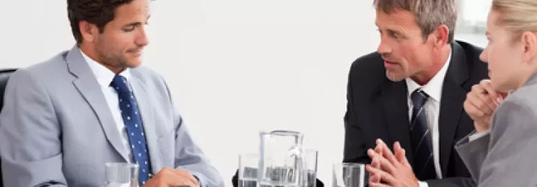 Personas en una reunión de negocios con trajes formales alrededor de una mesa.