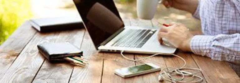 Persona trabajando en un portátil al aire libre, sosteniendo una taza de café.