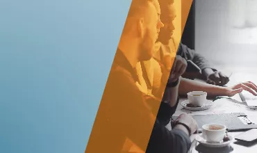 Personas en una reunión de trabajo con laptops y tazas de café.