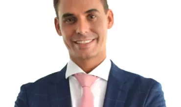 Persona con traje azul y corbata rosa sonriendo.