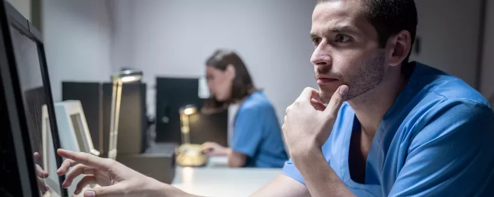 Profesional médico observa atentamente una pantalla en un entorno clínico.