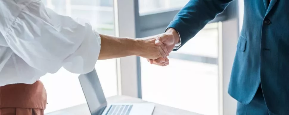 Dos personas dándose la mano junto a una laptop.