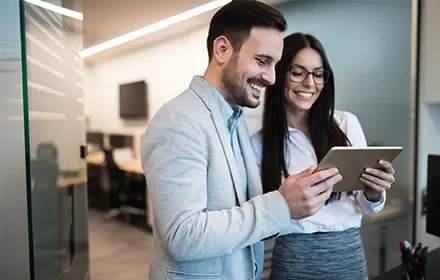 Dos personas sonriendo mientras miran una tablet en una oficina.