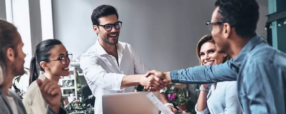 Grupo de personas en una reunión, dos están dándose la mano.